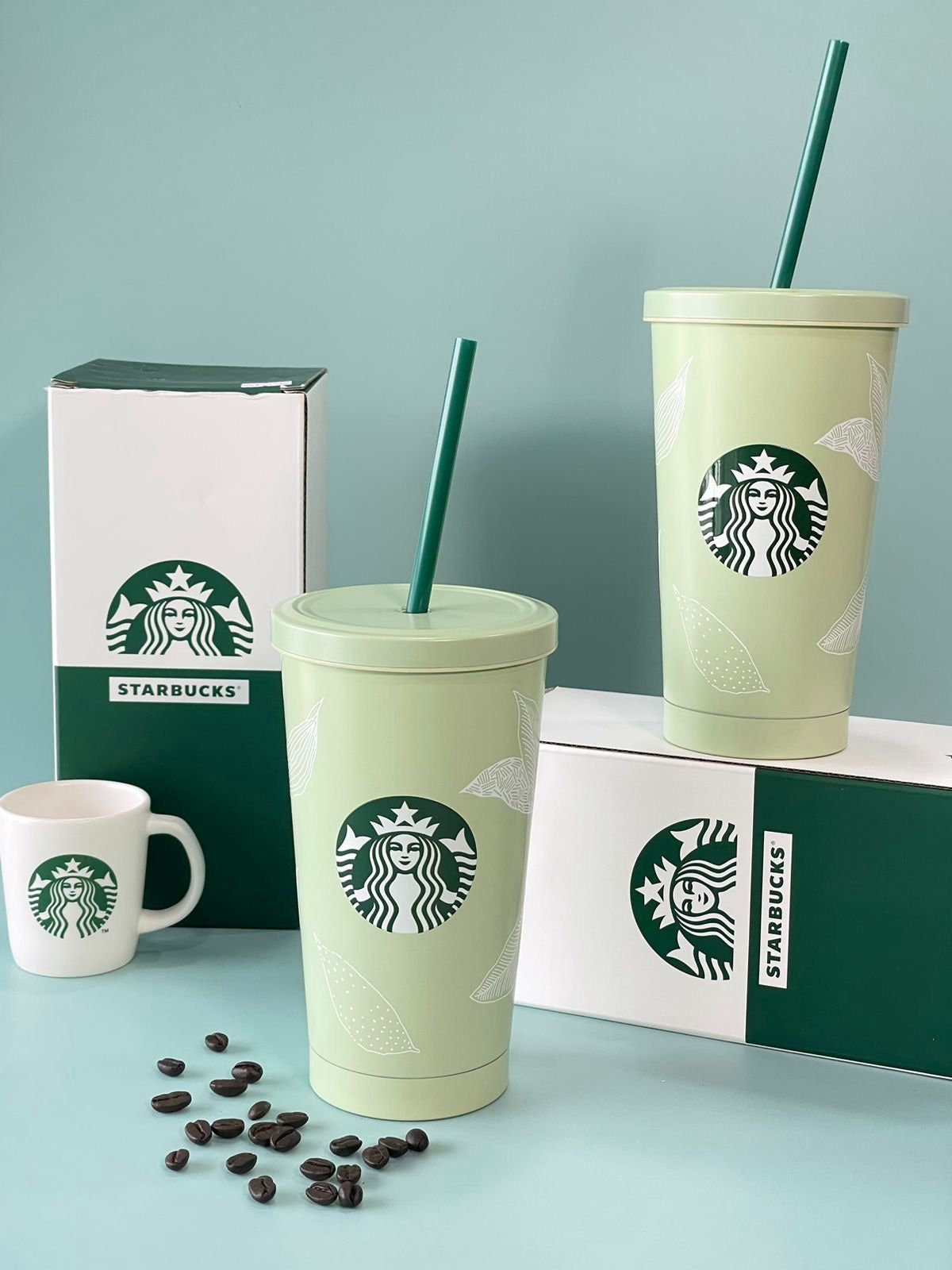 Starbucks cups with green lids and straws on a light blue background